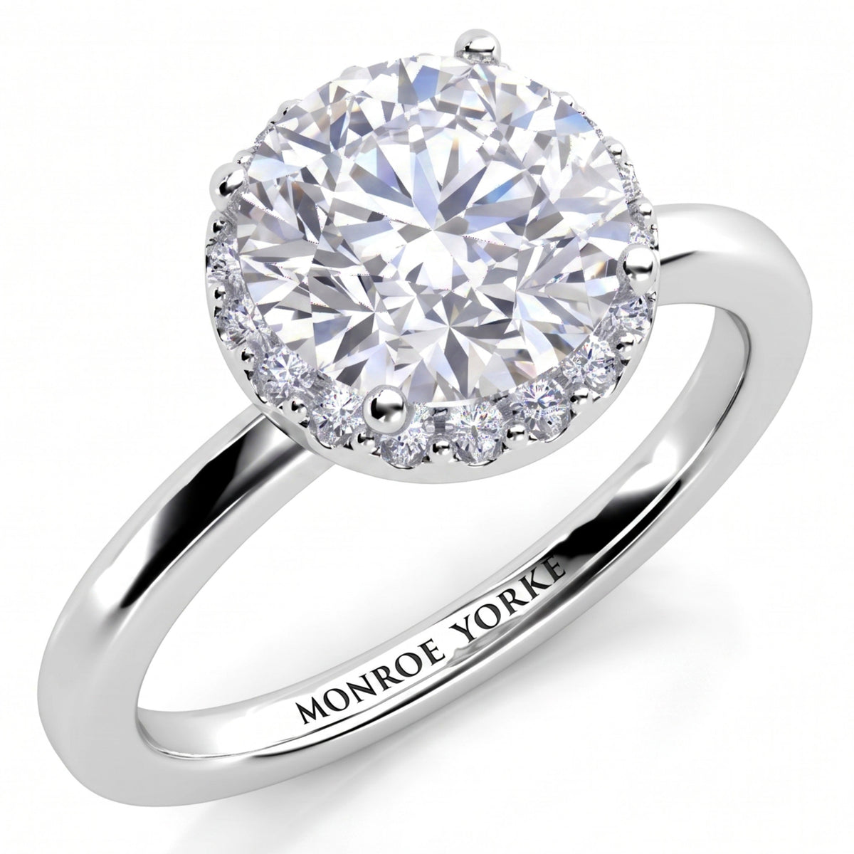 Alexa unique halo engagement ring in white gold or platinum, angled view of the round brilliant centre diamond with the halo set beneath it, Monroe Yorke engraved on the band.