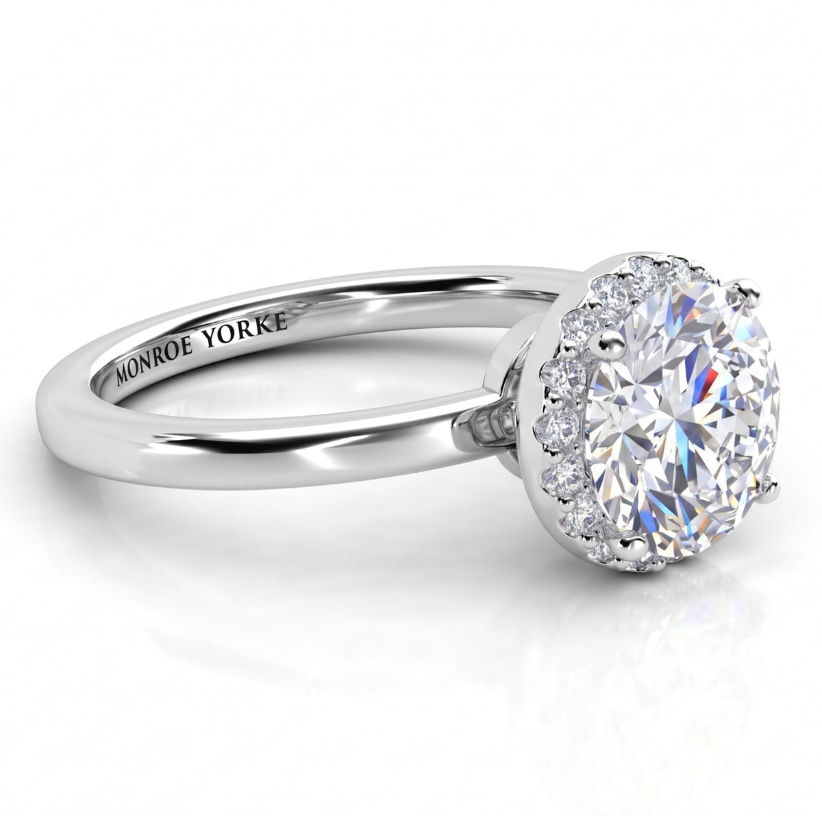Alexa unique halo engagement ring in white gold or platinum, low front view of the round centre diamond above a plain polished band.