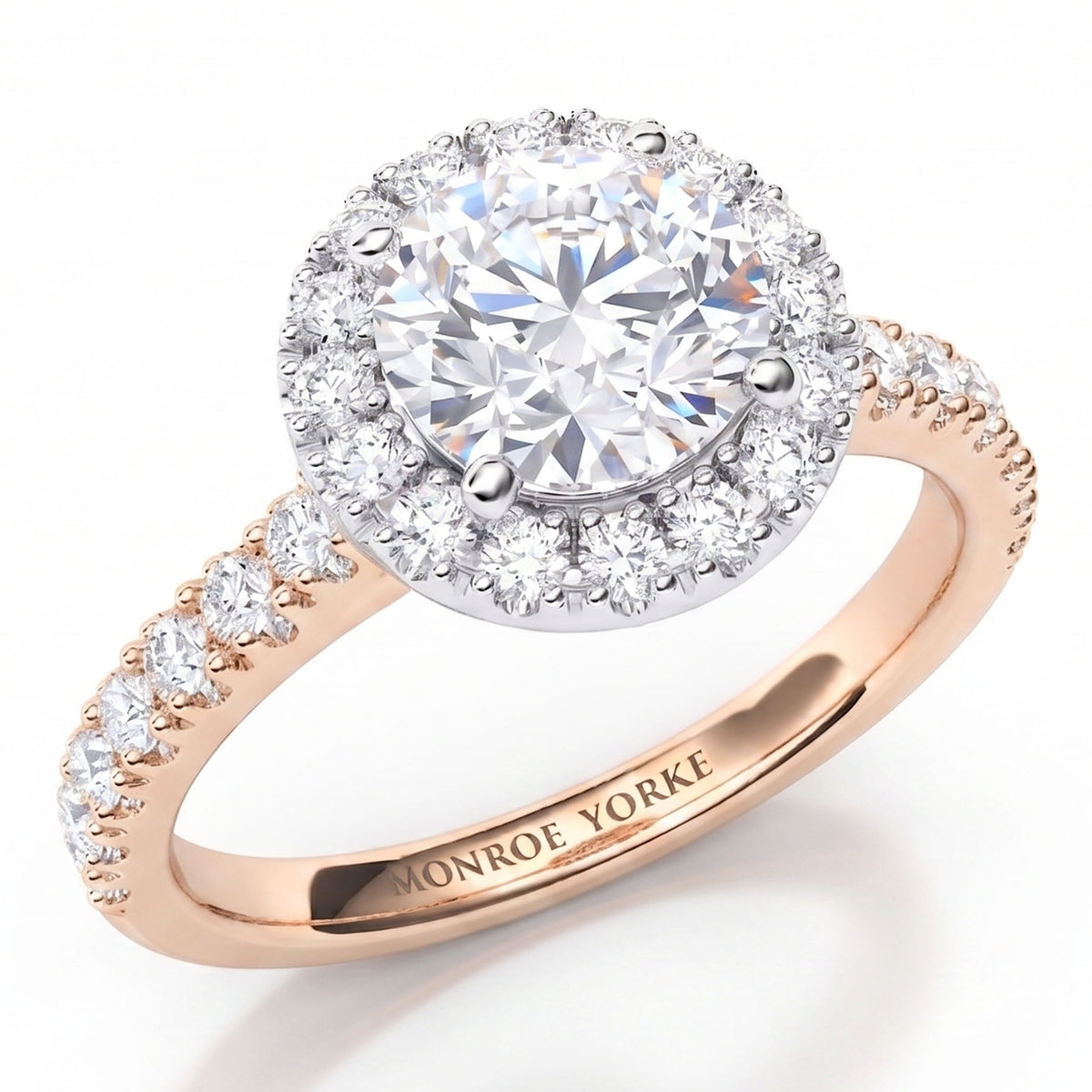 Ariana - a close-up studio shot of a ring with a large round clear centre stone surrounded by a halo of smaller clear stones, set on a rose gold band with pavé-set clear stones. The inside of the band is engraved with the brand name 'MONROE YORKE'.