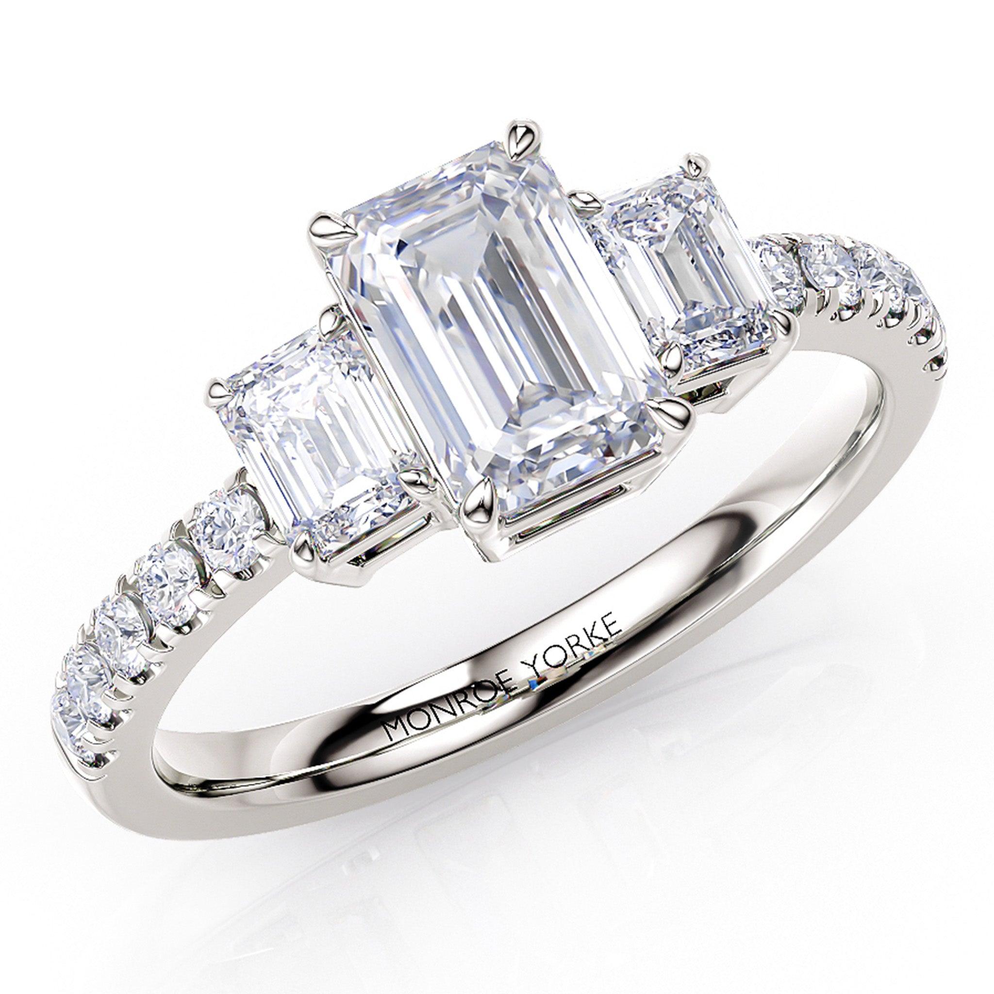 Adele emerald cut diamond trilogy ring in platinum. Three diamond ring with emerald cut diamonds and diamonds down the band. Created in platinum.