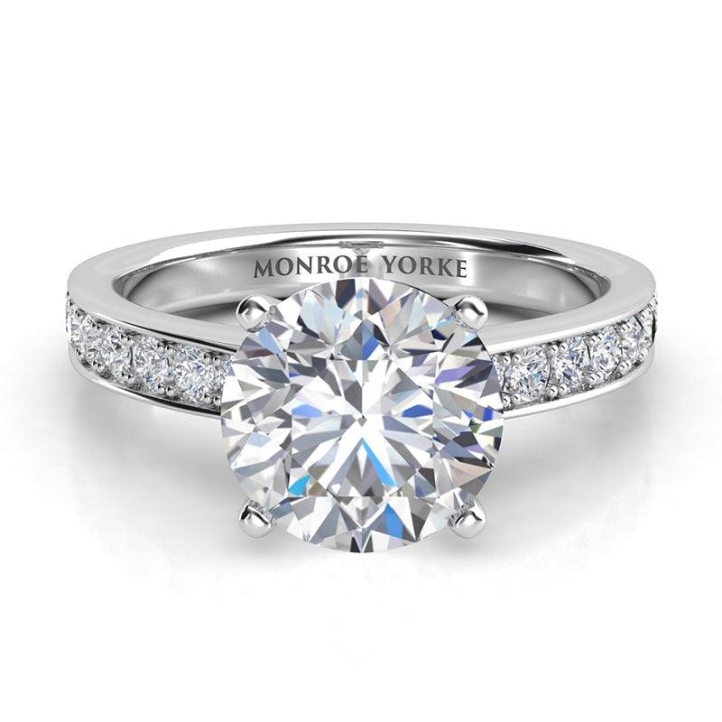 Danae - Platinum Round diamond ring in a 4 claw setting with pave set diamonds on the sweep up band. Front view.