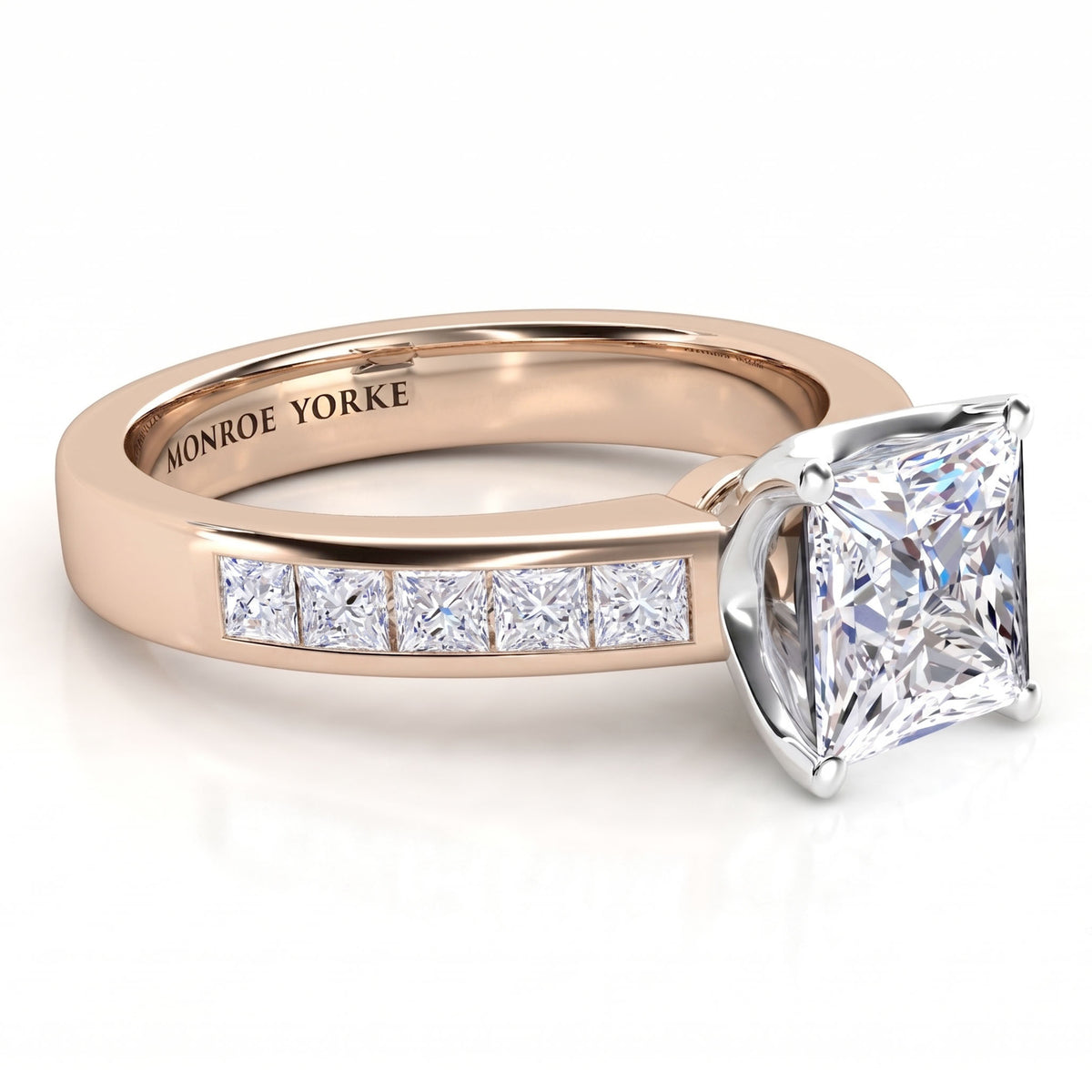 A princess-cut diamond engagement ring in rose gold with a channel set princess cut diamonds on the band, set against a clean white background. The inside of the band is engraved with 'MONROE YORKE'.