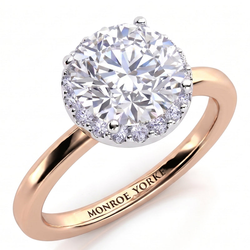 Alexa unique halo engagement ring in rose gold, angled view of the round brilliant centre diamond with the halo set beneath it, Monroe Yorke engraved on the band.
