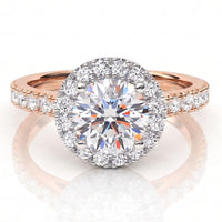 A round halo engagement ring featuring a large round-cut centre stone surrounded by a halo of smaller stones, set on a rose gold band with pavé accents, shown on a reflective white surface.