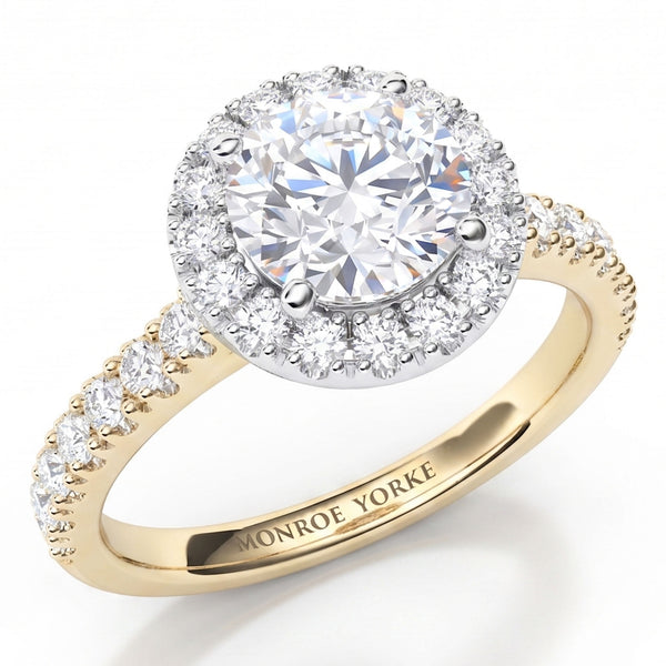 Ariana - a yellow gold  halo engagement ring featuring a round brilliant-cut centre stone surrounded by a halo of smaller diamonds, with a shank paved with small round diamonds. 