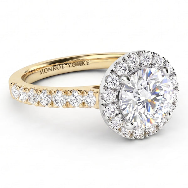 A Monroe Yorke diamond ring with a round-cut centre stone in a halo setting, a yellow gold band with pavé diamonds, and a silver-coloured diamond halo. The ring is photographed on a clean white background.