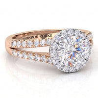 A close-up studio shot of a Monroe Yorke diamond engagement ring. The ring features a large round-cut centre diamond surrounded by a halo, set in a rose gold band with pavé diamonds on the shank, shown on a clean white background with a soft reflection.
