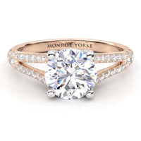 A Monroe Yorke diamond engagement ring featuring a round brilliant-cut center stone in a four-prong setting, with a rose gold split shank paved with small diamonds.