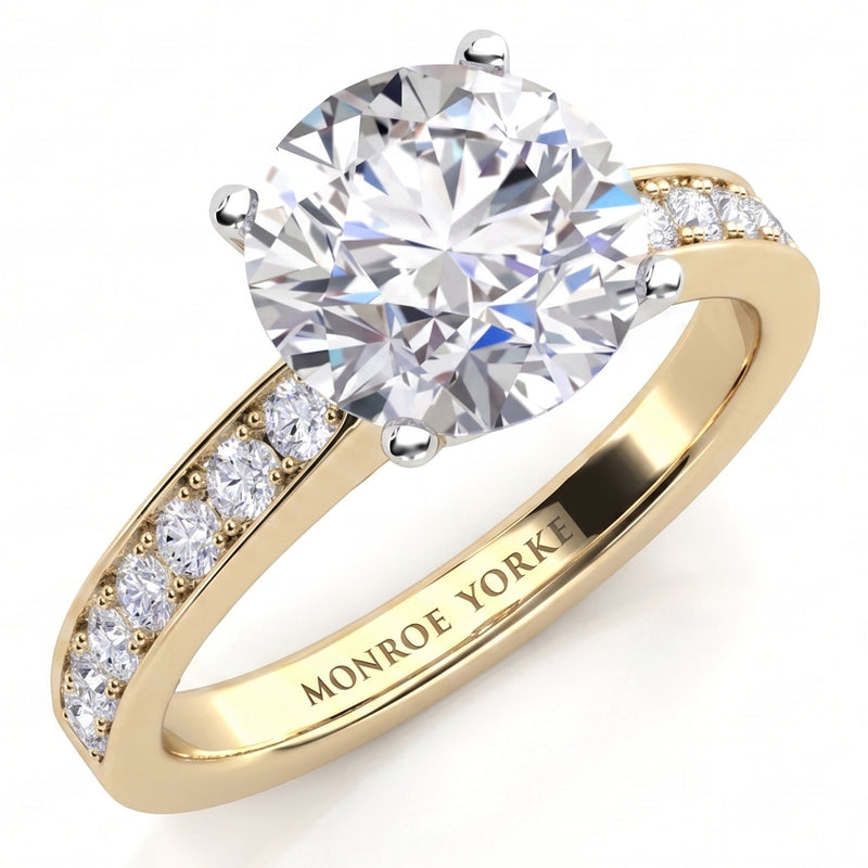 Danae engagement ring in yellow gold. Round brilliant centre diamond in a four claw setting with pave-set shoulder diamonds, MONROE YORKE engraved inside the band.