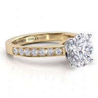 Danae engagement ring in yellow gold. Round brilliant centre diamond above a row of pave-set diamonds.