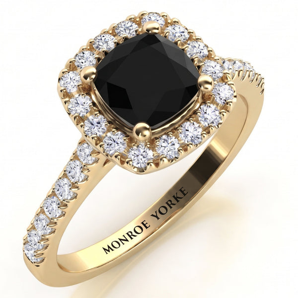 Darcie - yellow gold halo ring featuring a cushion-cut black centre stone and surrounded by a halo of diamonds and diamonds on the band, with the brand name 'MONROE YORKE' engraved on the band.