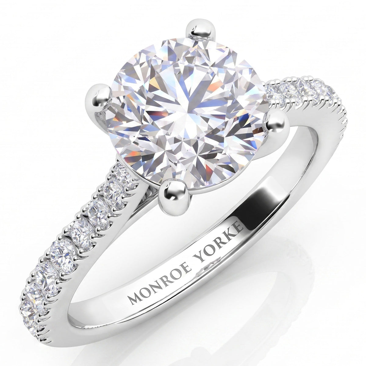 Enya engagement ring in white gold or platinum, round brilliant centre diamond in a four claw setting above a band of micro claw set accent diamonds.