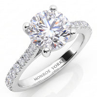 Enya engagement ring in white gold or platinum, round brilliant centre diamond in a four claw setting above a band of micro claw set accent diamonds.