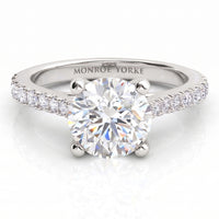 Enya engagement ring in white gold or platinum, round centre diamond in a four claw setting with diamonds on the sweep up band.