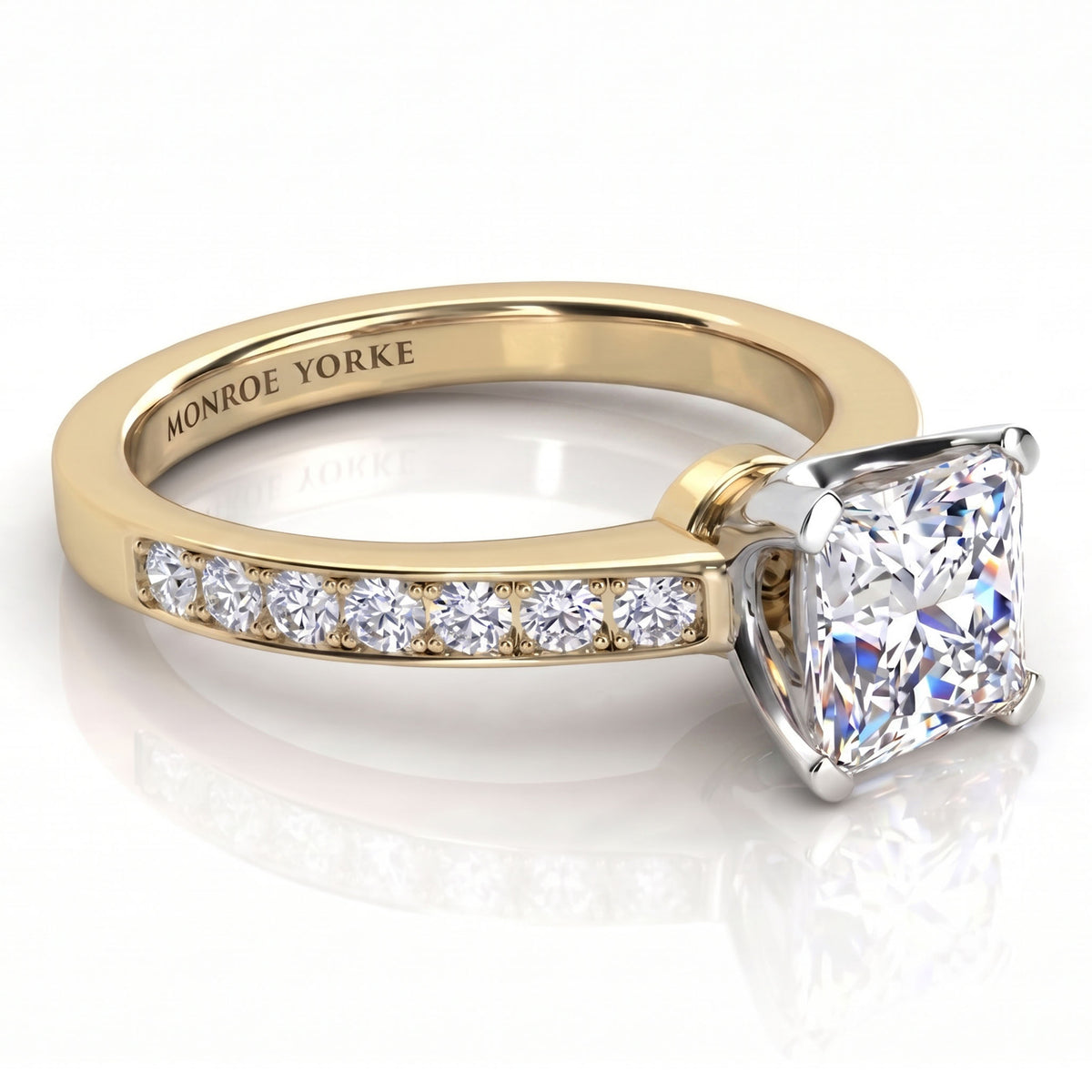 Fifth Avenue yellow gold engagement ring, princess cut centre diamond above a row of small round diamonds on the band.
