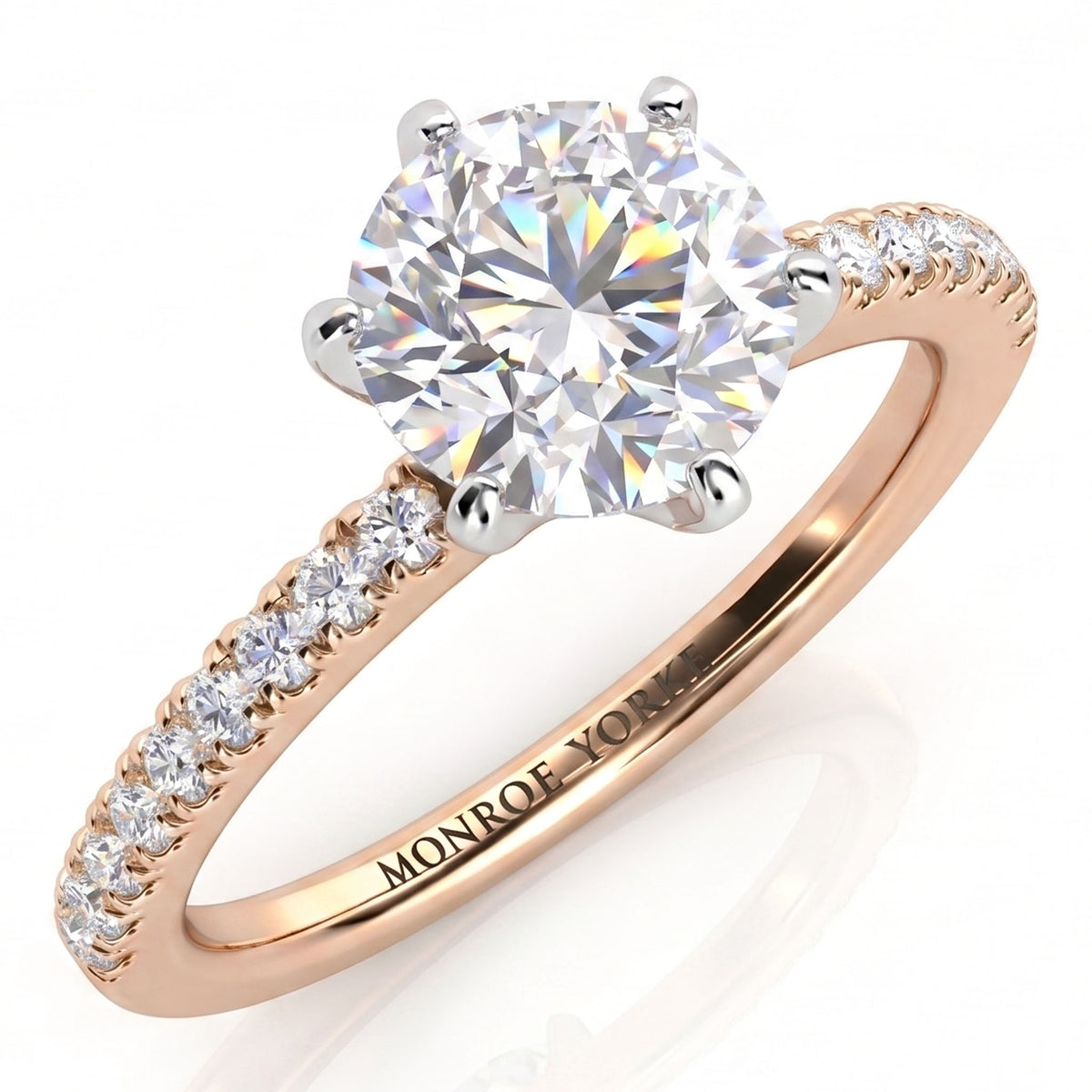 A rose gold solitaire engagement ring with a round brilliant-cut diamond center stone in a six claw setting and a pavé-set diamond band.
