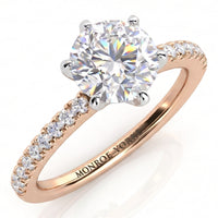 A rose gold solitaire engagement ring with a round brilliant-cut diamond center stone in a six claw setting and a pavé-set diamond band.