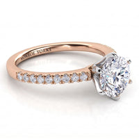 A rose gold diamond engagement ring with a round brilliant-cut center stone and a row of pavé diamonds on the band.