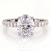 An oval-cut diamond engagement ring with a white gold or platinum band set with small round diamonds,