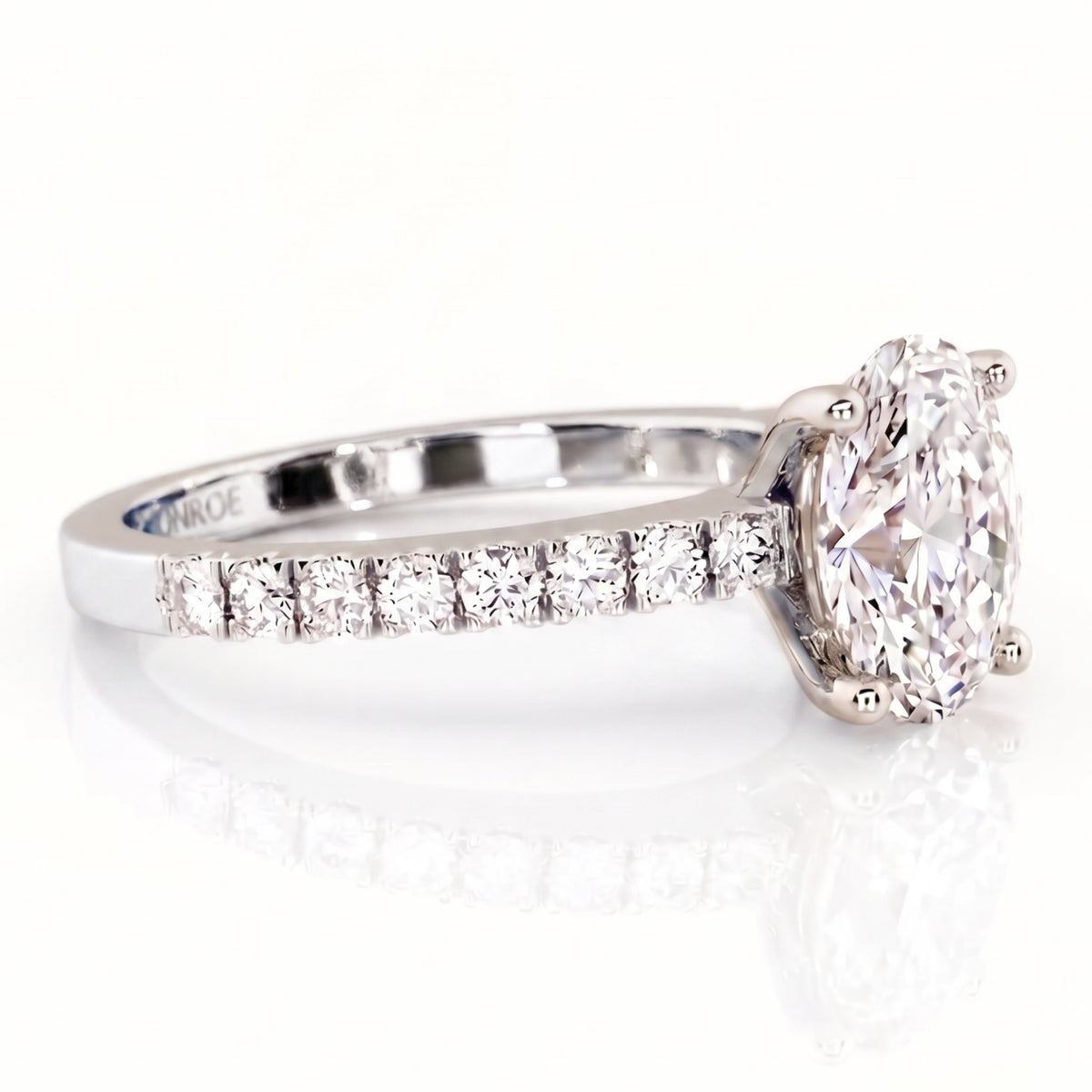 An oval diamond engagement ring in a white gold or platinum band with a row of smaller diamonds on the shank.
