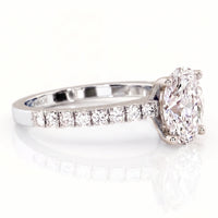 An oval diamond engagement ring in a white gold or platinum band with a row of smaller diamonds on the shank.