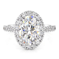 An oval halo engagement ring in white gold or platinum - featuring a large brilliant-cut center stone surrounded by a halo of smaller round stones, set on a diamond-cut band with pavé accents, shown on a white background.