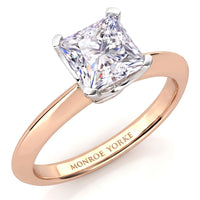 A princess cut diamond engagement ring in a rose gold band with a white metal prong setting, featuring the engraved brand name 'MONROE YORKE' on the inside of the band, set against a clean white background.