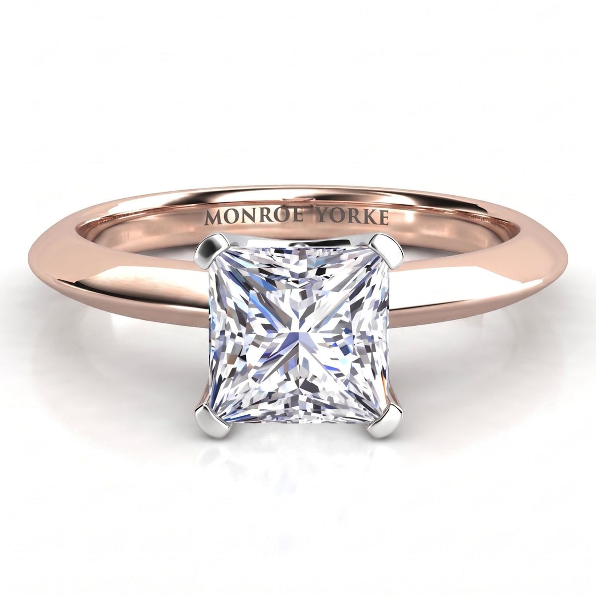 A princess cut diamond solitaire ring set in a rose gold band, with the brand name 'MONROE YORKE' engraved on the inside of the band. The ring is shown on a clean white background with a soft reflection.