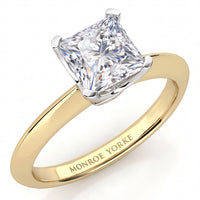 A classic princess cut diamond engagement ring in a yellow gold band with a white metal prong setting. The inside of the band is engraved with the brand name 'MONROE YORKE'.