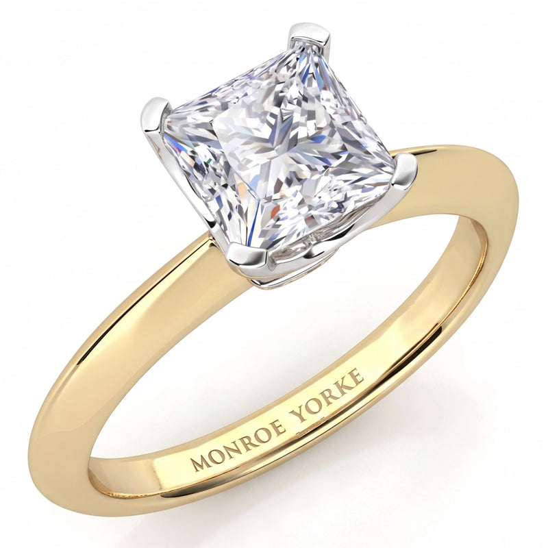 A classic princess cut diamond engagement ring in a yellow gold band with a white metal prong setting. The inside of the band is engraved with the brand name 'MONROE YORKE'.