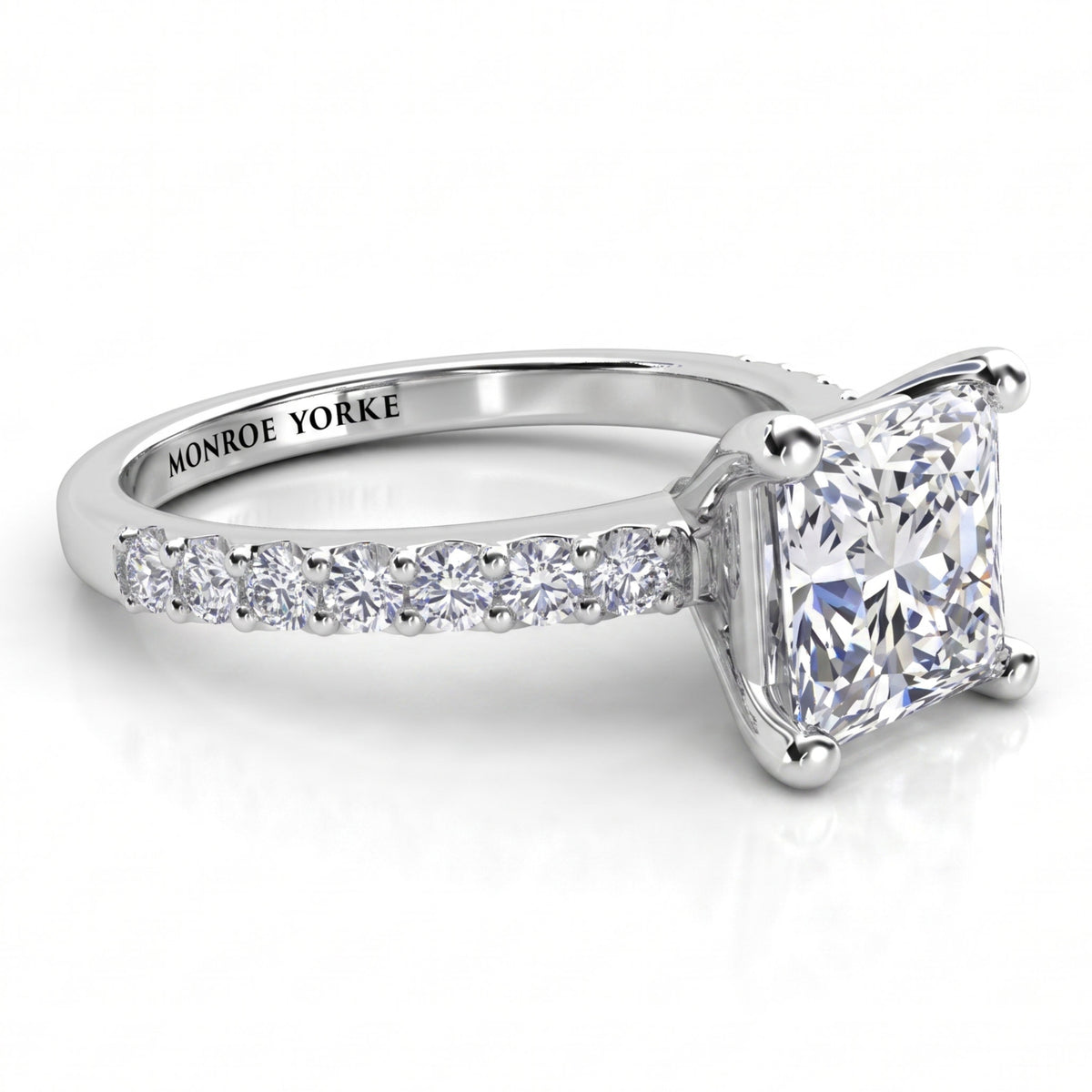 Lutèce engagement ring in white gold or platinum, low side view showing the princess cut centre diamond and the diamond set shoulders.