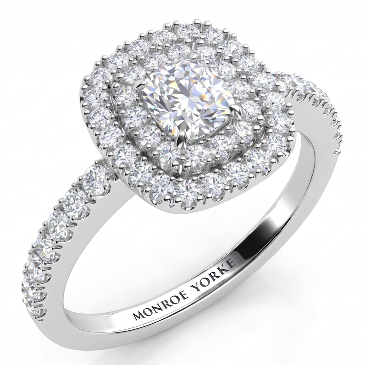 Norah double halo cushion cut engagement ring in white gold or platinum, angled view of the cushion cut centre diamond framed by two diamond halos, with round diamonds claw set down the band.