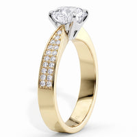 A yellow gold solitaire engagement ring with a pavé-set row of clear stones on the shank, featuring a brilliant-cut diamond center stone in a silver-colored prong setting, shown on a white background.