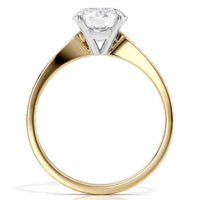 A classic solitaire engagement ring featuring a round brilliant-cut diamond set in a four-prong  setting, mounted on a polished yellow gold band, shown against a solid white background.
