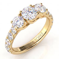 A yellow gold three-stone ring with round brilliant-cut diamonds, featuring smaller diamonds along the band a