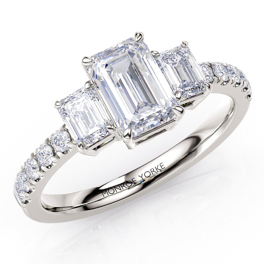 Adele emerald cut diamond trilogy ring in platinum.  Three diamond ring with emerald cut diamonds and diamonds down the band.  Created in platinum.