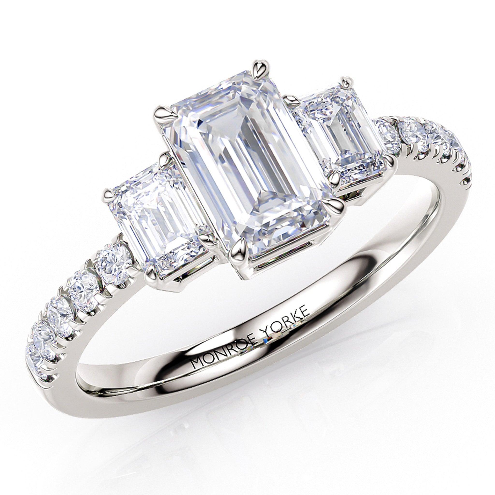 Aspen emerald cut diamond trilogy ring with diamonds on the band. 18 carat white gold.
