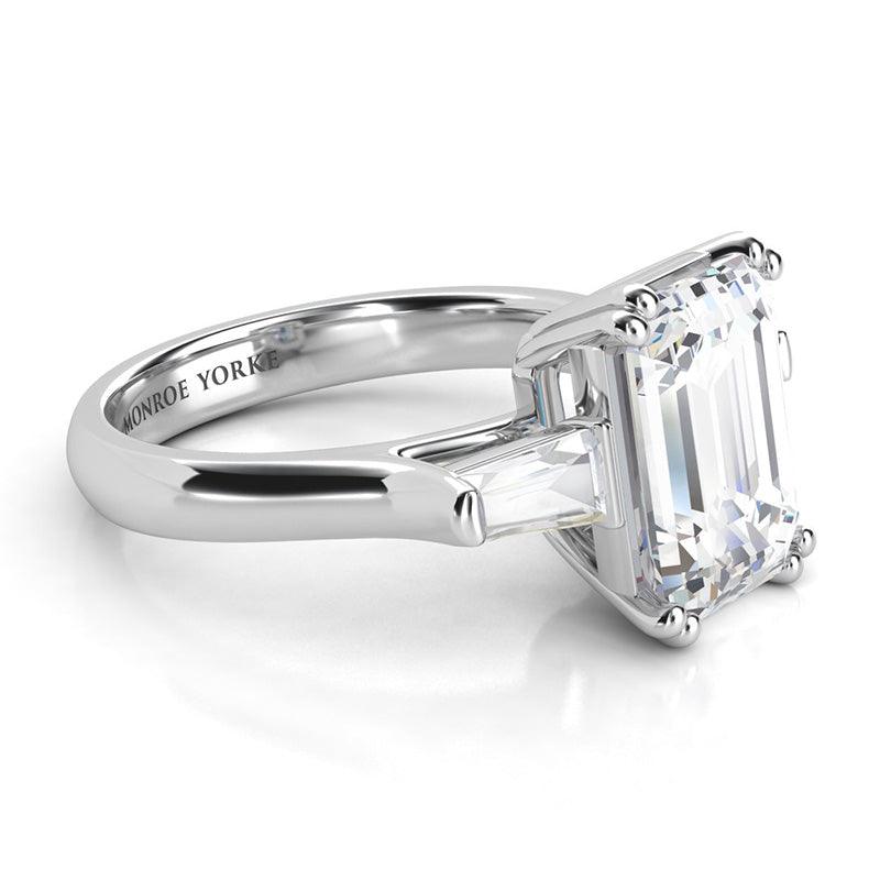 Envy Platinum - Emerald cut diamond and tapered cut baguette three stone ring.  Centre emerald cut diamond held in double claws. Side view