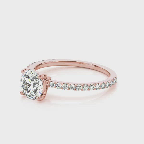 A rose gold engagement ring that adds that extra flair to the classic solitaire design. A round brilliant cut diamond is claw set in a masterfully crafted ring. The rose gold band is then blanketed with shimmering diamond accents making sure that this ring glistens like the April rains.
